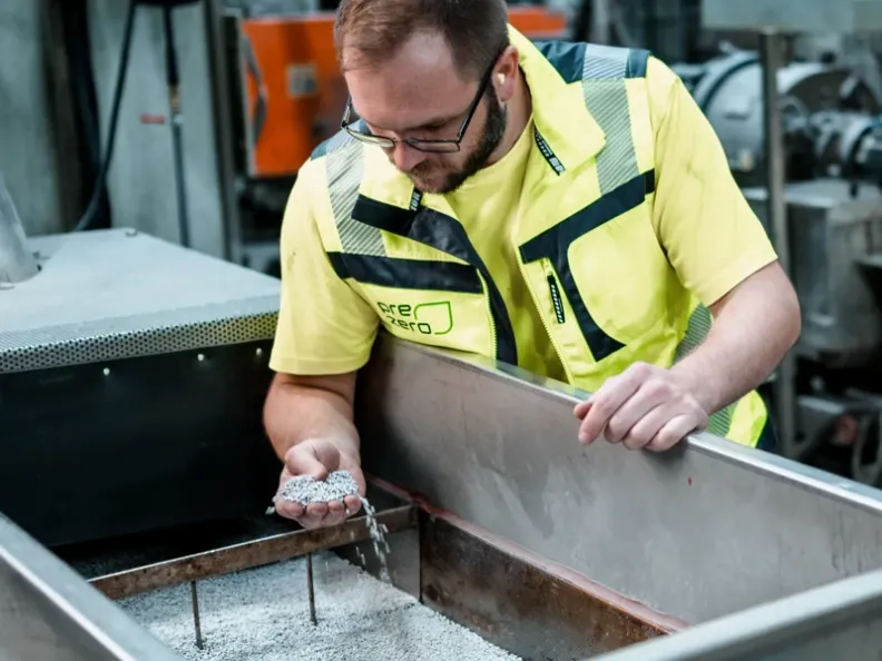 PreZero Recycling: Ein Mitarbeiter in Warnweste prüft hochwertiges, graues Kunststoffgranulat für die Kreislaufwirtschaft