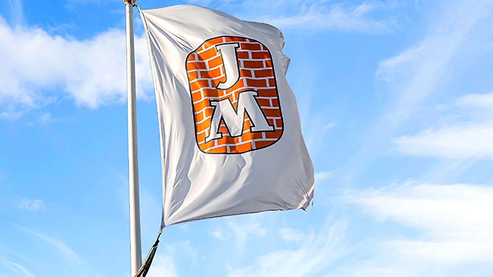 Flagga med JM:s logotyp på vajar mot blå himmel