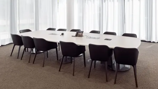 Großer weißer Konferenzraumtisch mit schwarzen Polsterstühlen in einem hellen Raum mit Fensterfront