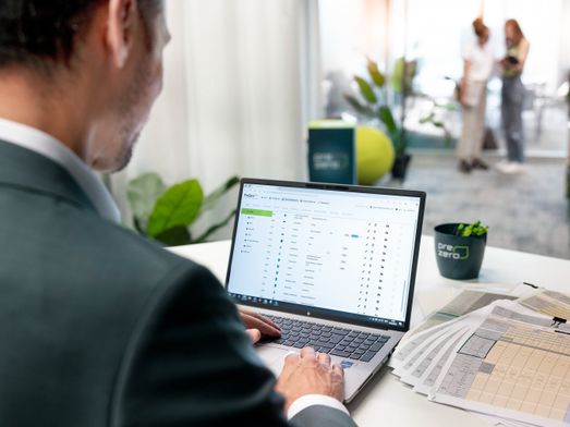 Mitarbeiter arbeitet im Büro am Laptop mit einer PreZero-Software, daneben liegen gedruckte Tabellen.