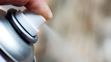 Toppen av sprayburk, finger som trycker ner knappen och sprayar