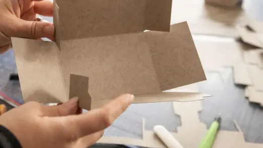 Hände falten eine nachhaltige Verpackung aus Graspapier der Marke OutNature zur Demonstration umweltfreundlicher Materialalternativen bei PreZero