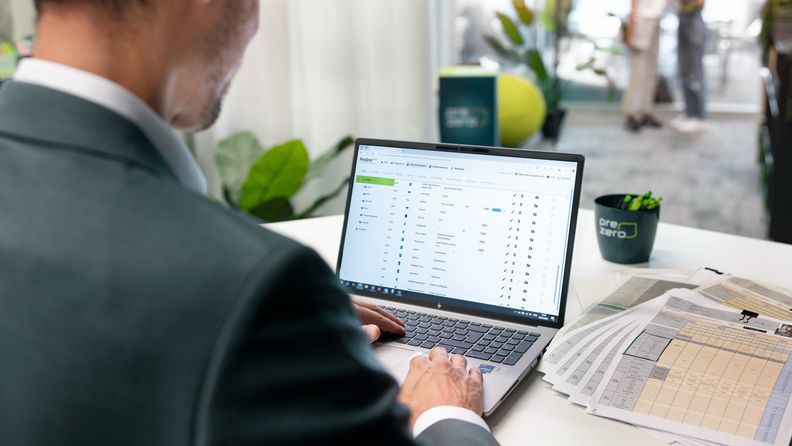 Mitarbeiter arbeitet im Büro am Laptop mit einer PreZero-Software, daneben liegen gedruckte Tabellen.