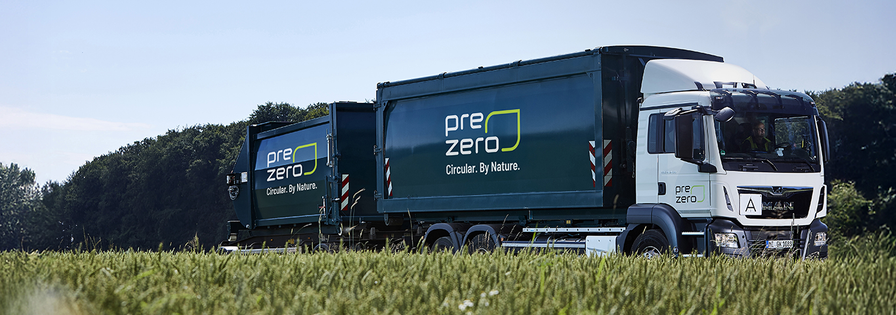 Weiß-grüner prezero LKW mit zwei Containern fährt an einem Getreidefeld und Waldrand vorbei