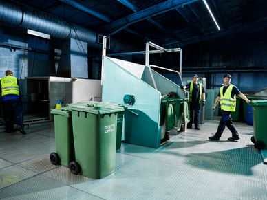 Three employees empty trash can in plant