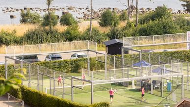 Padelbana vid strandkant med fyra spelare, sedda på avstånd