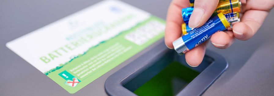Hand wirft Batterien in Sammelbehälter