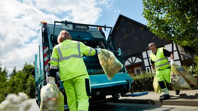 Employees with yellow working clothes throw garbage bags into truck in a residential area