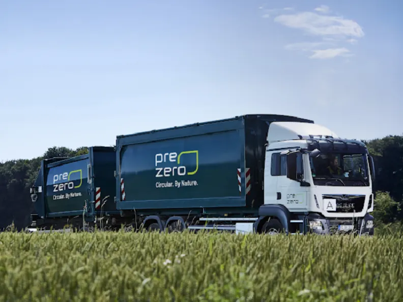Weiß-grüner prezero LKW mit zwei Containern fährt an einem Getreidefeld und Waldrand vorbei