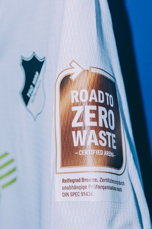 Weißes Fußballtrikot mit Nachhaltigkeits-Badge auf dem Ärmel: "ROAD TO ZERO WASTE - CERTIFIED ARENA