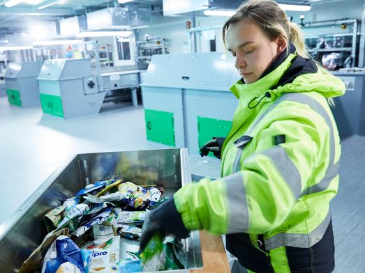 Employee sorts plastic waste in metal box and in the background are machines