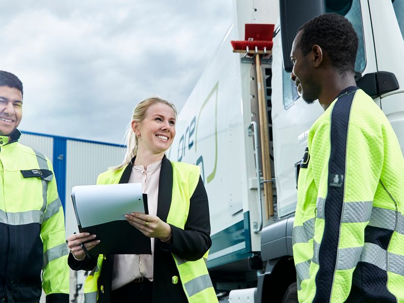 Three persons with security vest are discussing in front of a PreZero truck
