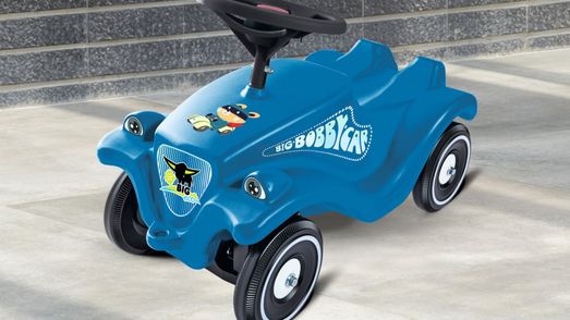 Blaues Bobby Car auf grauem Fließenboden vor grauer Steinwand