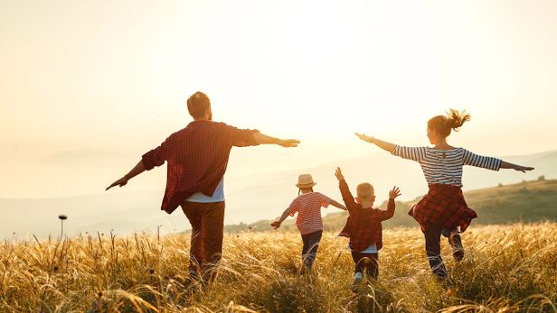 Pappa, mamma och två barn springer på fält i solnedgång