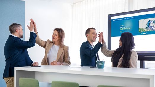 Vier Teammitglieder geben sich High-Fives im PreZero-Büro vor einem Monitor mit Marken-Logo.