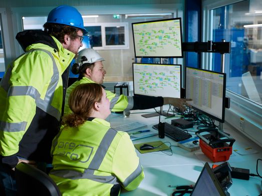 Three blue collar workers look at drawings on computer in office