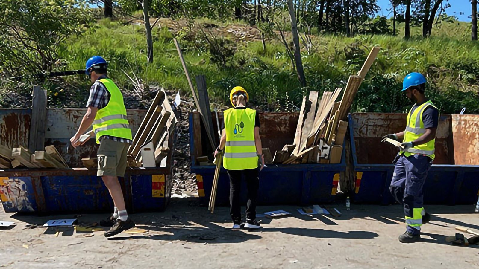 Människor i säkerhetsvästar och hjälmar som sorterar brädor