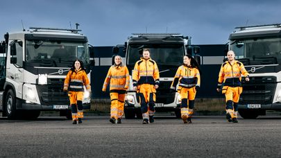 Fem miljöarbetare går emot oss, i bakgrunden fronterna på tre lastbilar