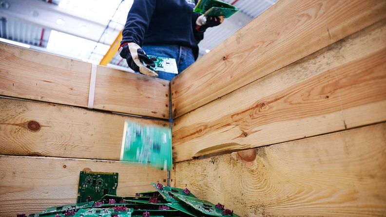 Arbeiter in Schutzhandschuhen wirft grüne Leiterplatten in eine große Holzkiste zum Recycling.