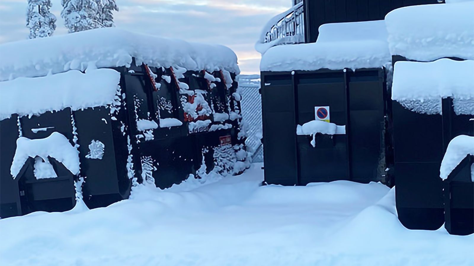 Gröna containrar med snö på och runt sig, det vill säga att snöröjning inte skötts