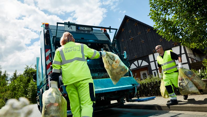 Employees with yellow working clothes throw garbage bags into truck in a residential area