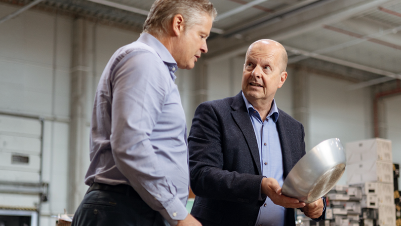 Two men in business attire inspecting a metal bowl in a large warehouse or industrial facility