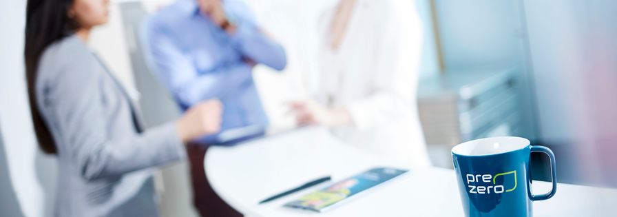 Three employees discussing in the background and in the foreground a PreZero cup