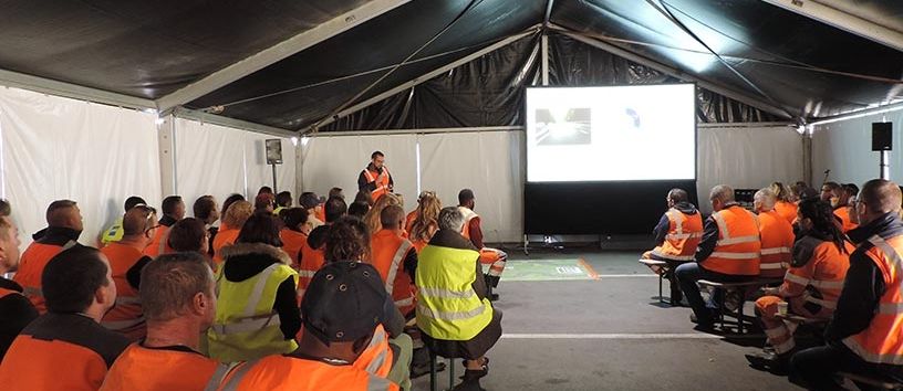 Personnel de Lamesch en gilets de sécurité assistant à une formation sur la sécurité au travail sous un chapiteau.