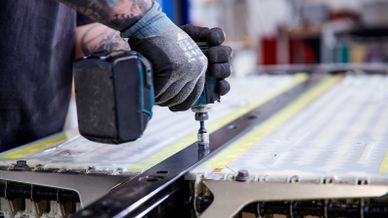Ein Mechaniker in Schutzhandschuhen demontiert mit einem Akku-Schlagschrauber eine Schiene an einem Batterie-Modul.