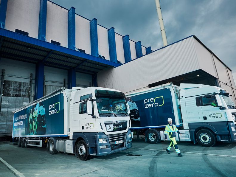 Two PreZero trucks in front of a building while one employee walks out between them