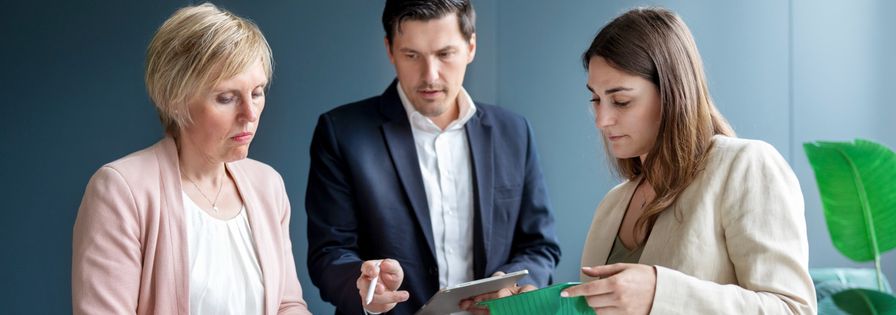 Drei Geschäftsleute begutachten bei einem Meeting am Tisch verschiedene Verpackungsmaterialien aus Plastik und Pappe.