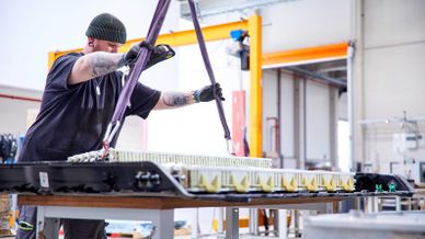 Mitarbeiter bewegt ein großes Batterie-Modul mithilfe von Hebegurten in einer Industriehalle.