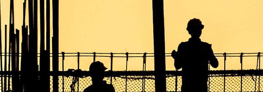 Svart siluett av byggarbetare på byggställning mot gul bakgrund
