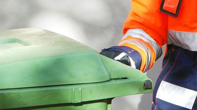 Detalj av person som hämtar grönt avfallskärl