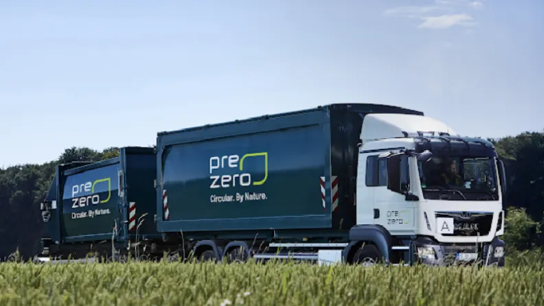Weiß-grüner prezero LKW mit zwei Containern fährt an einem Getreidefeld und Waldrand vorbei