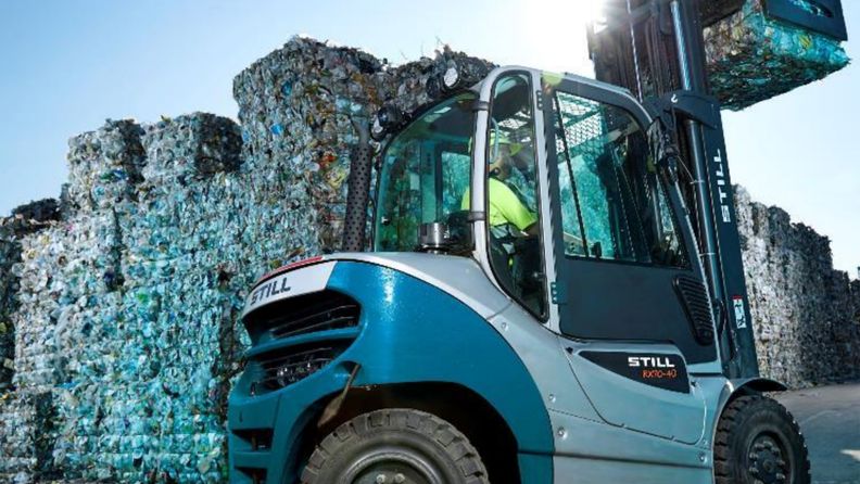Truck som kör bal inne på anläggning, flera balar i bakgrunden