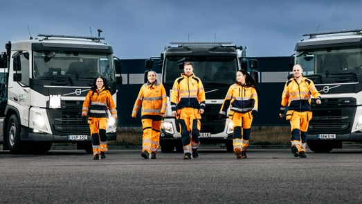 Fem miljöarbetare går emot oss, i bakgrunden fronterna på tre lastbilar