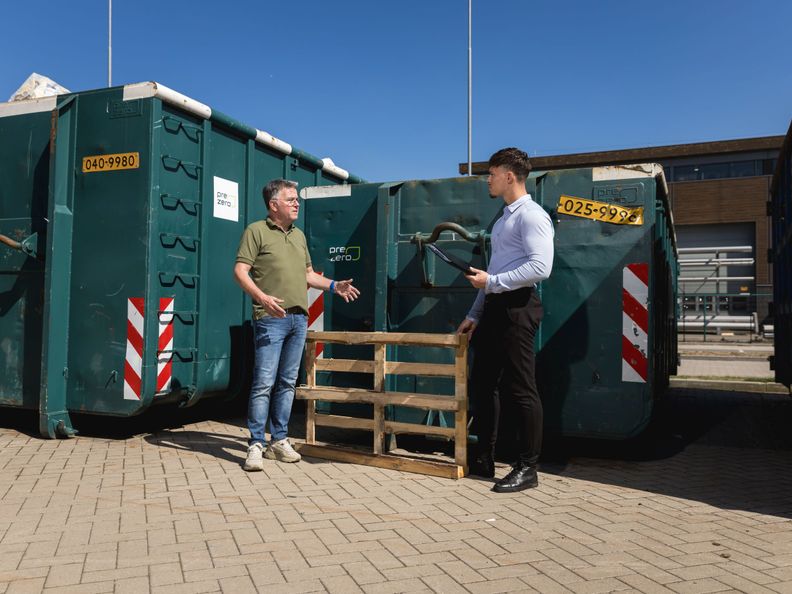 2 mannen staan voor groene containers te praten
