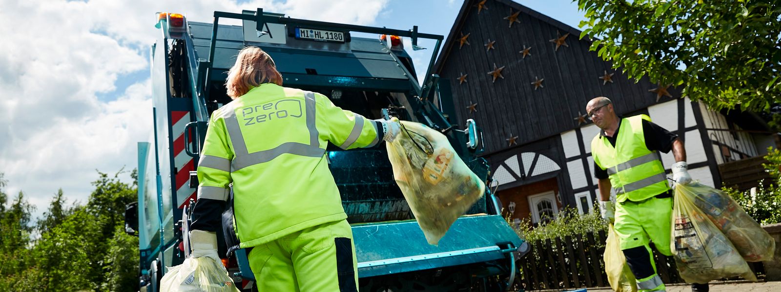 Employees with yellow working clothes throw garbage bags into truck in a residential area