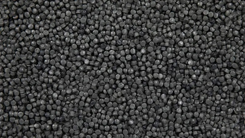 Close-up of densely packed dark gray plastic granules filling the entire frame