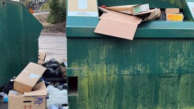 Överfylld container med avfall på marken, utanför containern