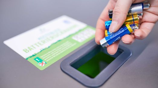Hand wirft Batterien in Sammelbehälter