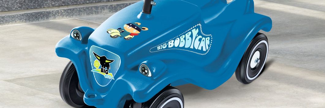 Blaues Bobby Car auf grauem Fließenboden vor grauer Steinwand