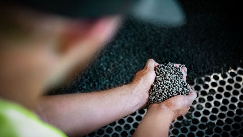 Person sedd snett bakifrån som i kupade händer håller plastpellets