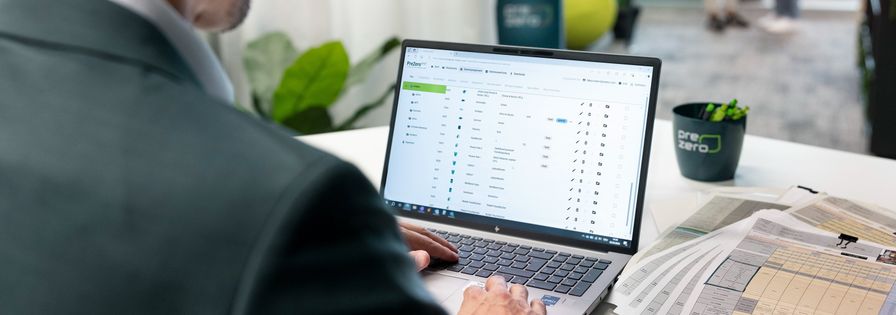 Mitarbeiter arbeitet im Büro am Laptop mit einer PreZero-Software, daneben liegen gedruckte Tabellen.