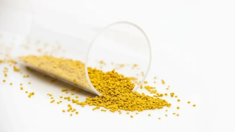 High-quality yellow rHDPE regranulate from PreZero pouring out of a measuring cylinder