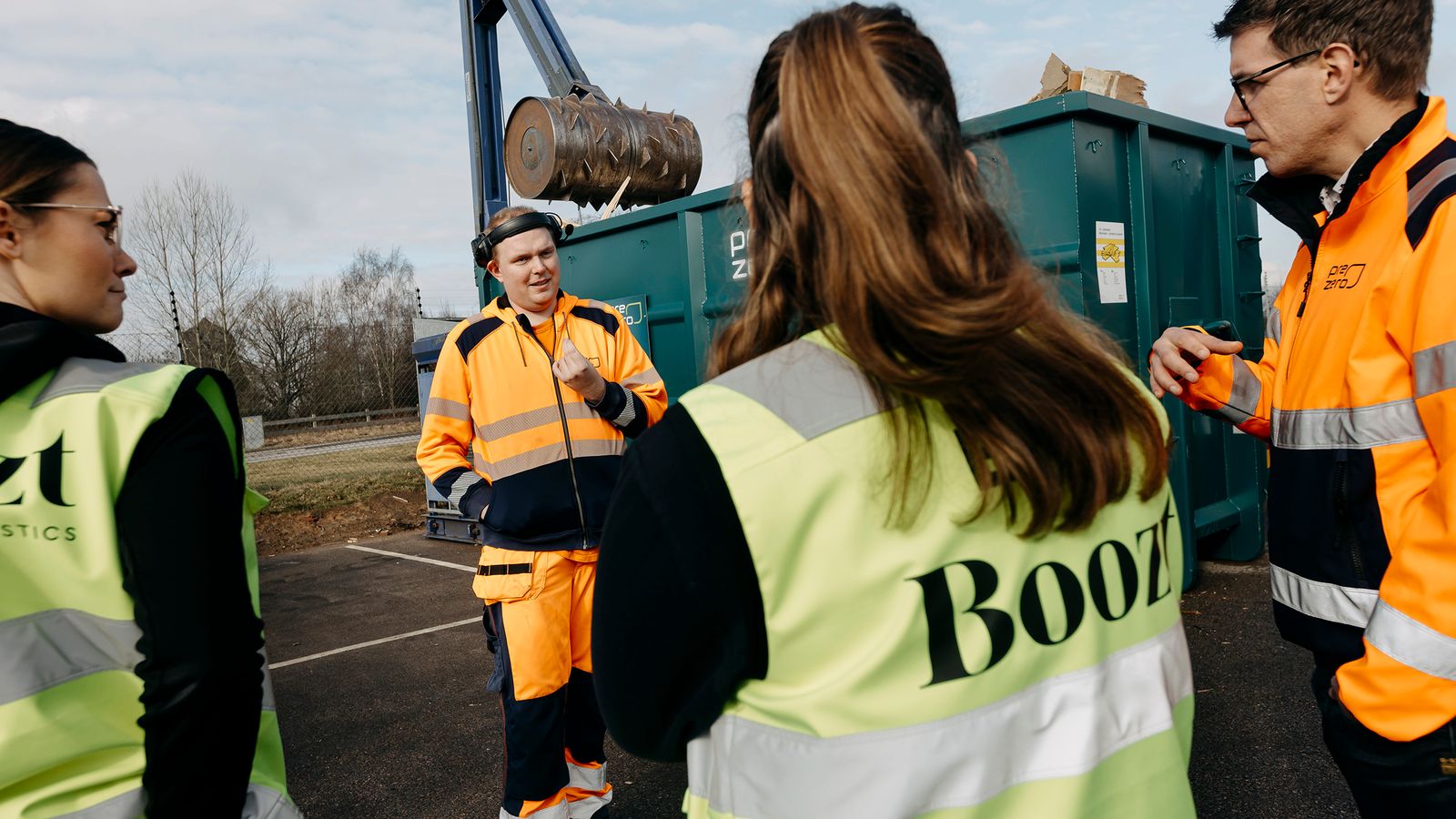 En PreZero-anställd berättar om källsortering vid container, tre personer som lyssnar