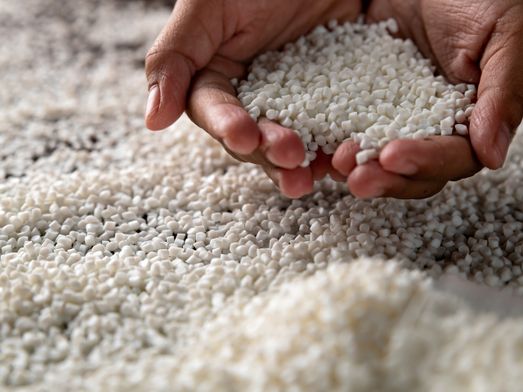Händer som visar vita plastpellets.