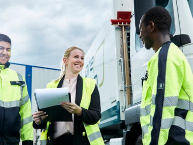 White collar employee with high visibility west talks to blue collar employee with working clothes in front of truck