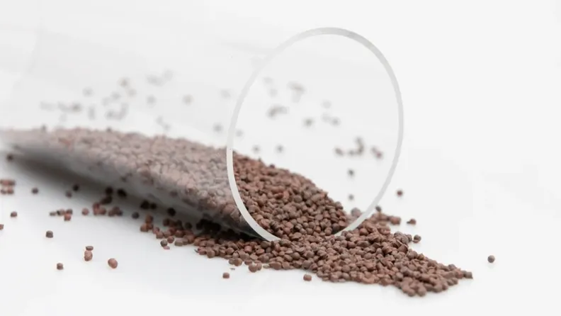 Brown plastic granules spilling out of an overturned transparent cylinder onto a white background